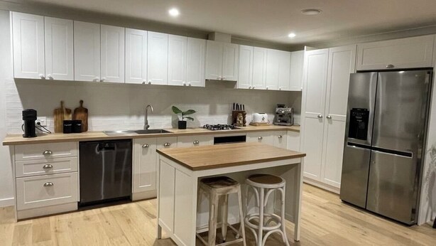 Una cocina moderna con armarios blancos, un refrigerador de acero inoxidable y una isla de madera con taburetes.