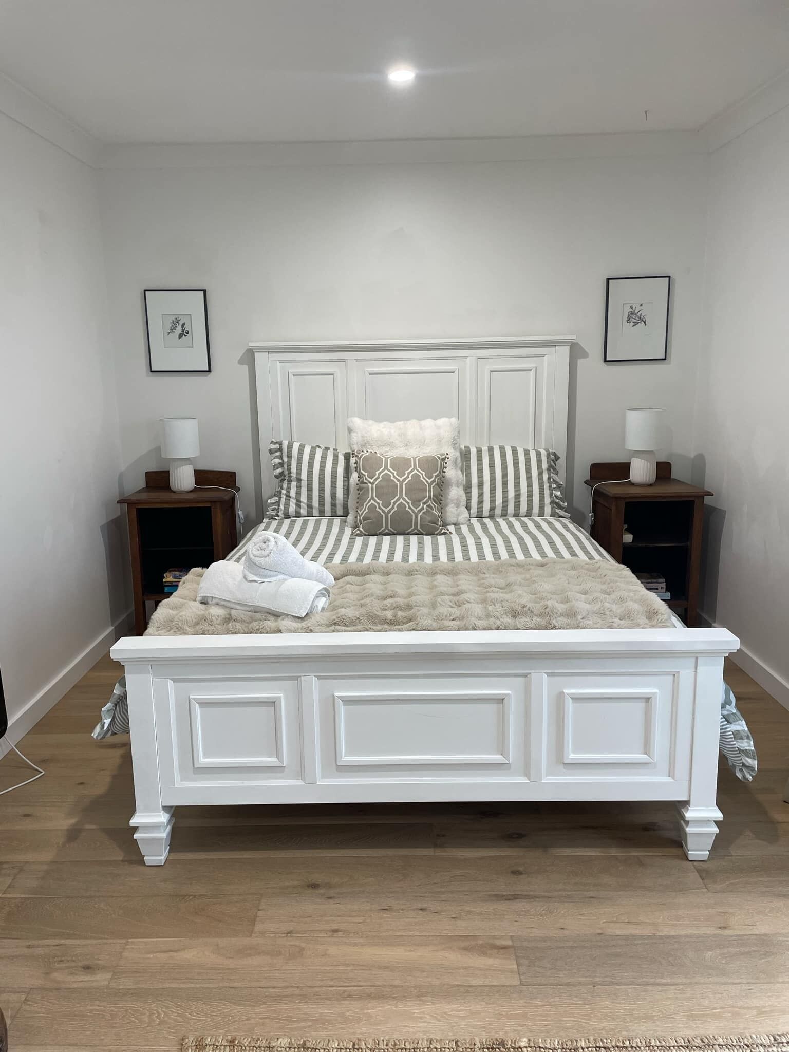 A white four-poster bed with a fluffy beige blanket, two bedside tables with lamps, and framed artwork on the walls.