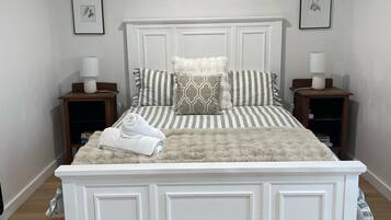 A white four-poster bed with a fluffy beige blanket, two bedside tables with lamps, and framed artwork on the walls.