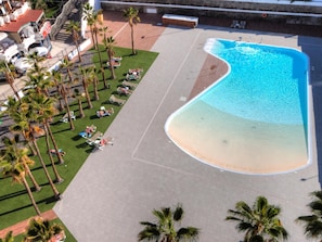 Eine Luftaufnahme eines Resorts mit einem großen Swimmingpool, Palmen und Liegestühlen.