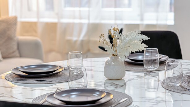 Une table à manger avec des assiettes, des verres et un vase contenant des fleurs séchées.