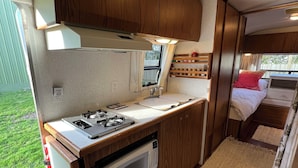 Cozinha compacta de motorhome, com fogão, micro-ondas e armários de madeira.