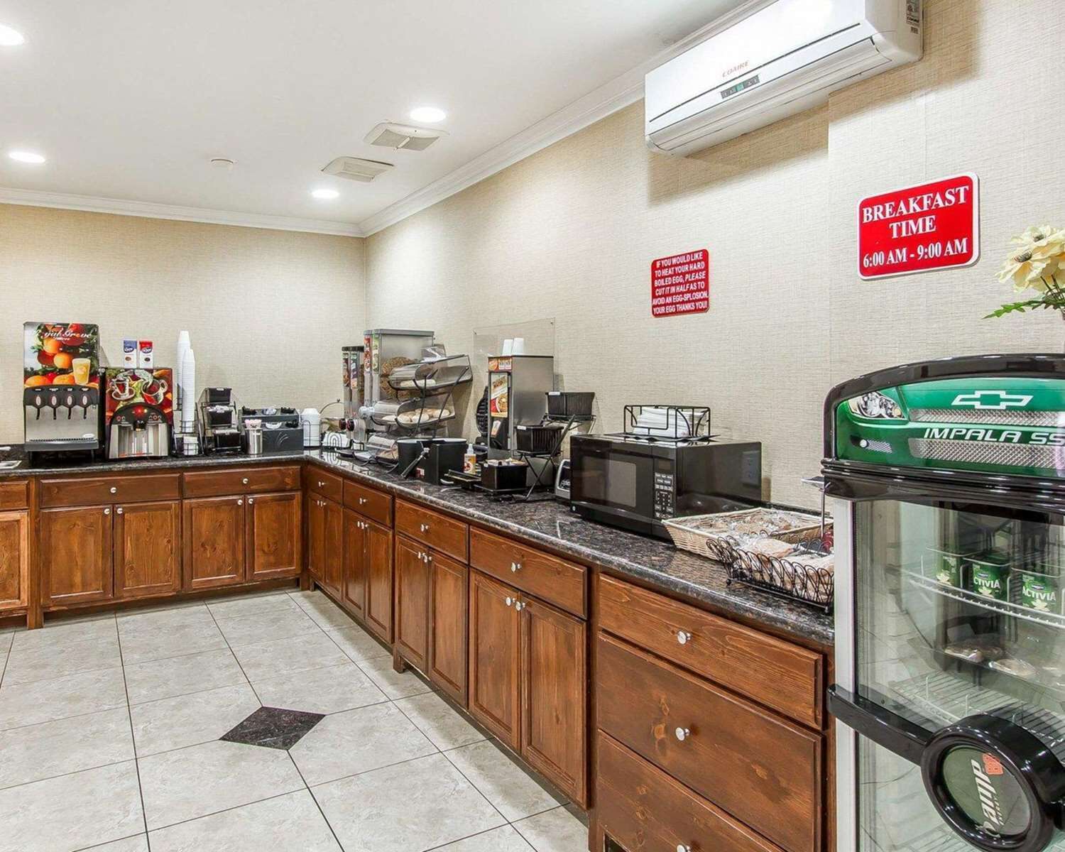 Une cuisine d’hôtel avec des placards en bois, un coin café et un panneau indiquant les heures du petit-déjeuner, de 6h00 à 9h00.