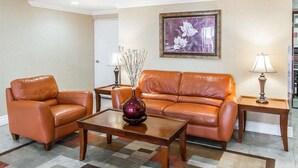 A hotel lobby with a brown leather sofa, two armchairs, a wooden coffee table, a vase with branches, a framed floral artwork, and two lamps on side tables. - Super 8 by Wyndham Mesa Downtown Near Convention Center (Mesa)