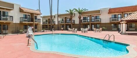 A pool area with a rectangular pool, lounge chairs, and palm trees.