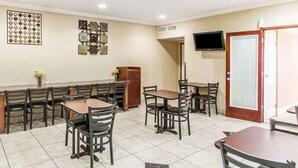 A dining area with a long table and chairs, a television mounted on the wall, and a door with a frosted glass panel. - Super 8 by Wyndham Mesa Downtown Near Convention Center (Mesa)
