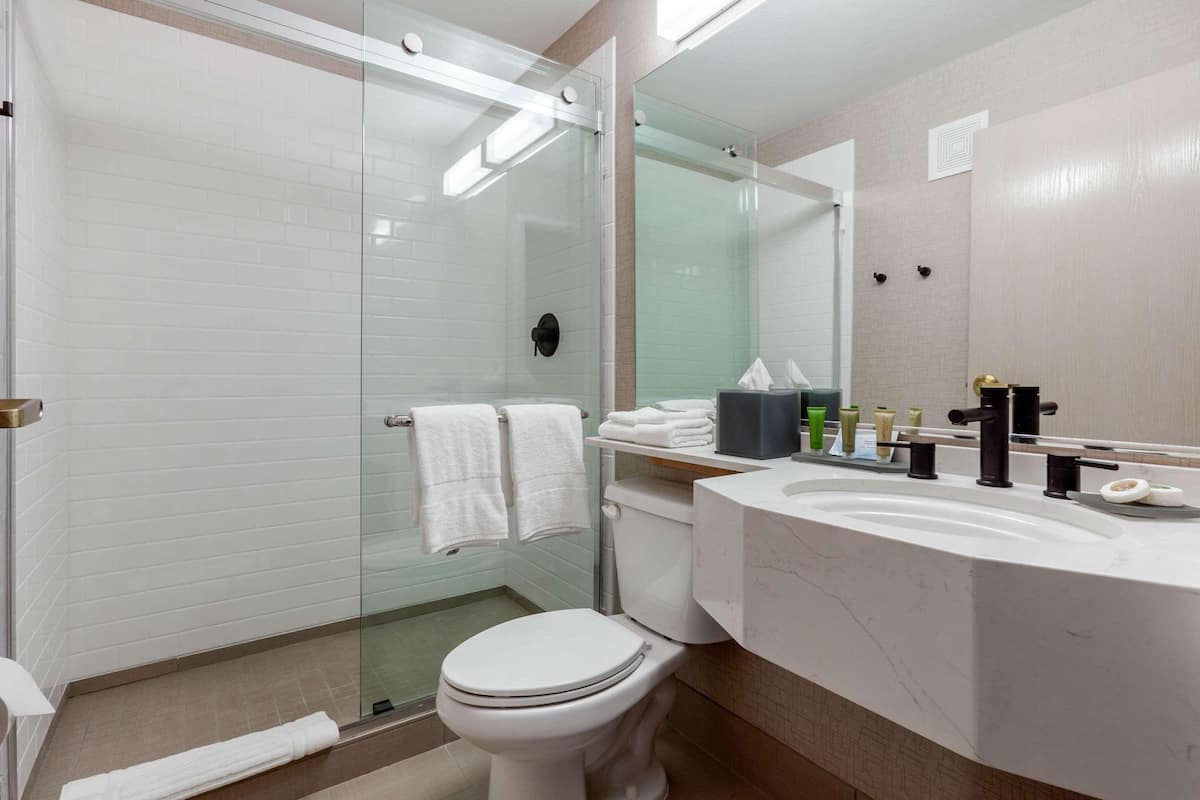 A modern bathroom with a glass-enclosed shower, a white toilet, and a marble sink with a mirror.