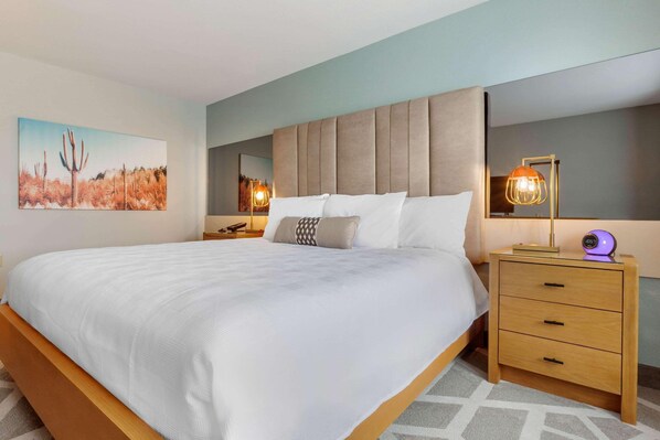 A bedroom with a large bed, a nightstand with a lamp, a wooden drawer, and a painting on the wall. - La Quinta Inn & Suites Tempe University / Phoenix (Tempe)