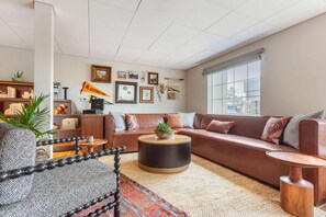 A living room with a sofa, a round coffee table, a patterned rug, and a bookshelf. - La Quinta Inn & Suites Tempe University / Phoenix (Tempe)
