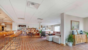 A spacious lobby with a tiled floor, a seating area with sofas and chairs, a reception desk, and a wall with framed pictures. - La Quinta Inn & Suites Tempe University / Phoenix (Tempe)