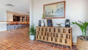 Un espace d’accueil doté d’un sol carrelé, d’une console en bois sur laquelle est posé un tableau noir, d’un tableau encadré et d’une plante en pot.