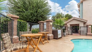 An outdoor pool area with a pool, a seating area with chairs and tables, and a building with a gated entrance. - La Quinta Inn & Suites Tempe University / Phoenix (Tempe)