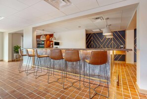 A modern bar area with a long counter, bar stools, and pendant lighting. - La Quinta Inn & Suites Tempe University / Phoenix (Tempe)