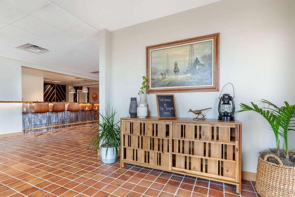 A reception area with a tiled floor, a wooden console with a chalkboard sign, a framed painting, and a potted plant. - La Quinta Inn & Suites Tempe University / Phoenix (Tempe)