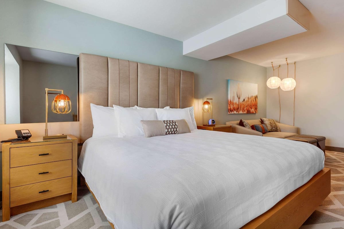 A modern bedroom with a large bed, bedside tables, a nightstand, and a wall-mounted lamp.