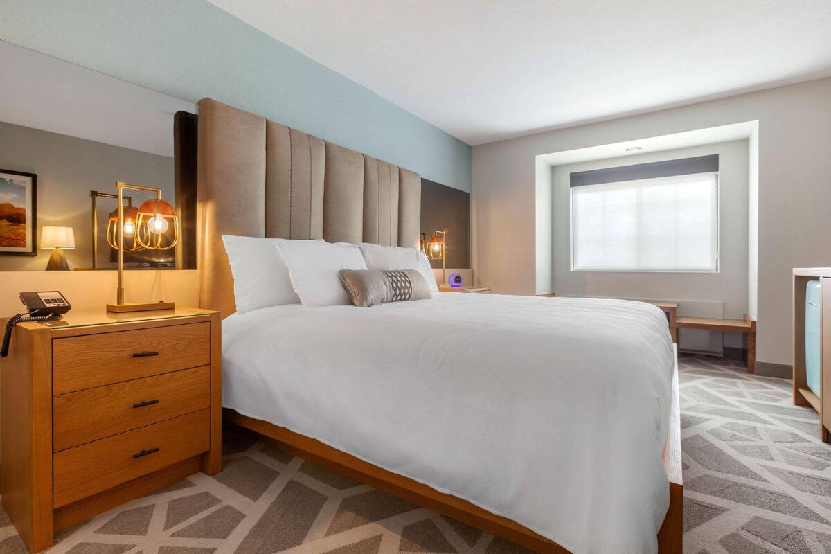 A hotel room with a large bed, bedside tables with lamps, a desk, and a window.