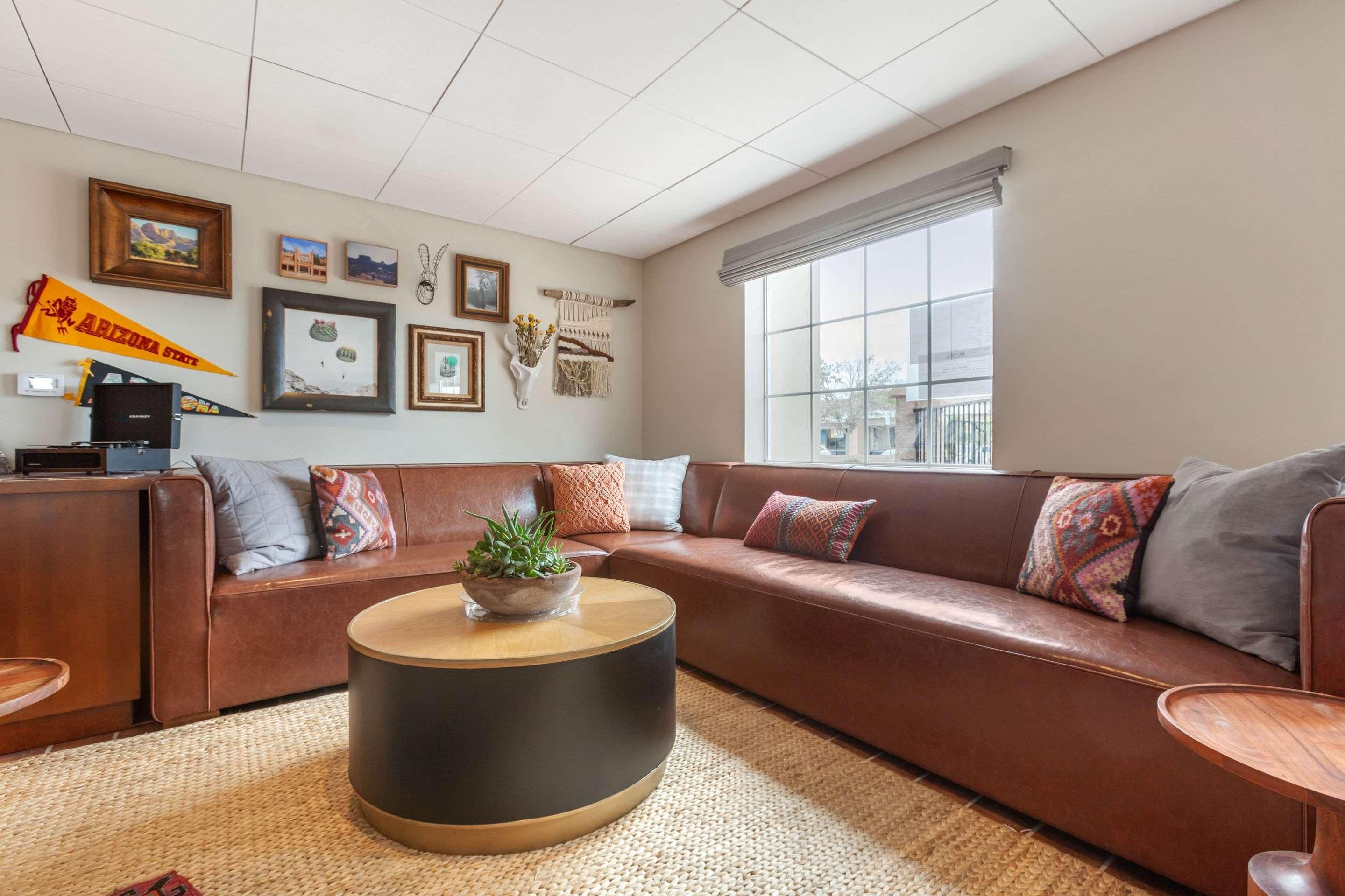 A living room with a brown leather sofa, a round coffee table, and a large window.