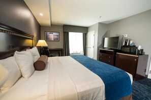 A hotel room with a large bed, a desk with a lamp, a television, and a minibar. - Comfort Suites Seabrook Kemah (Seabrook)