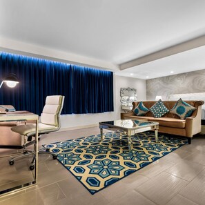 A modern living room with a sofa, a desk, and a patterned rug. - The Hills Hotel (Laguna Hills)