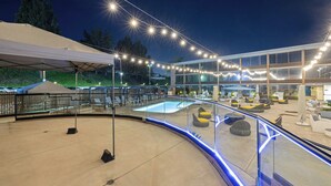 A poolside area with a glass railing, lounge chairs, and a covered seating area. - The Hills Hotel (Laguna Hills)