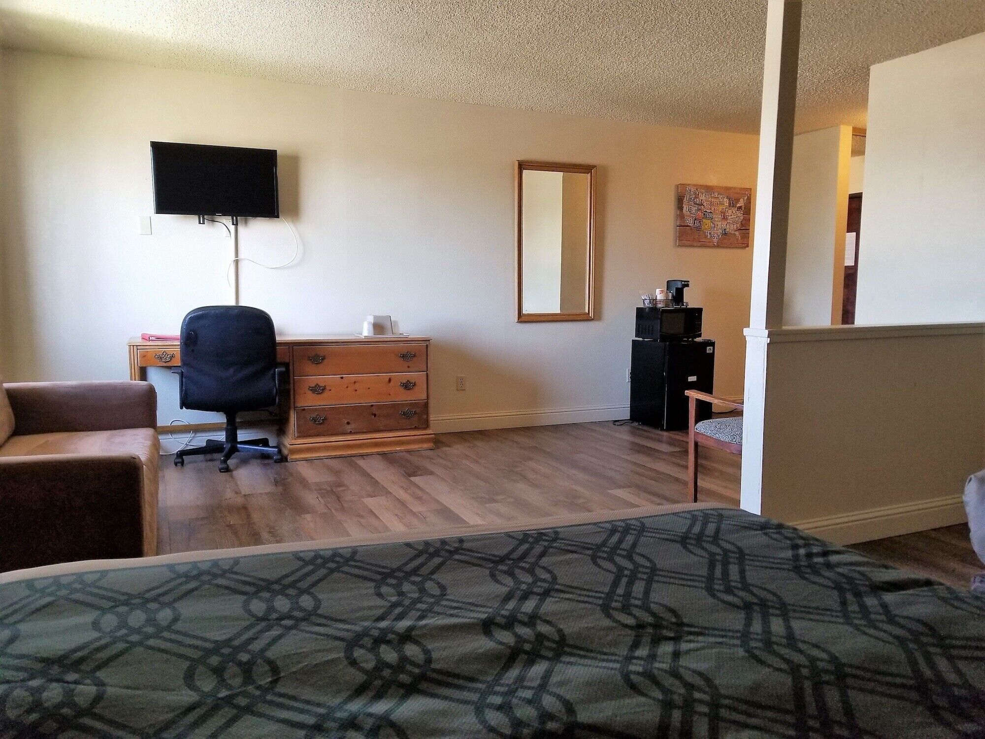 Une chambre d’hôtel comprenant un lit, un bureau avec une chaise, une commode, une télévision, un four à micro-ondes et un miroir.
