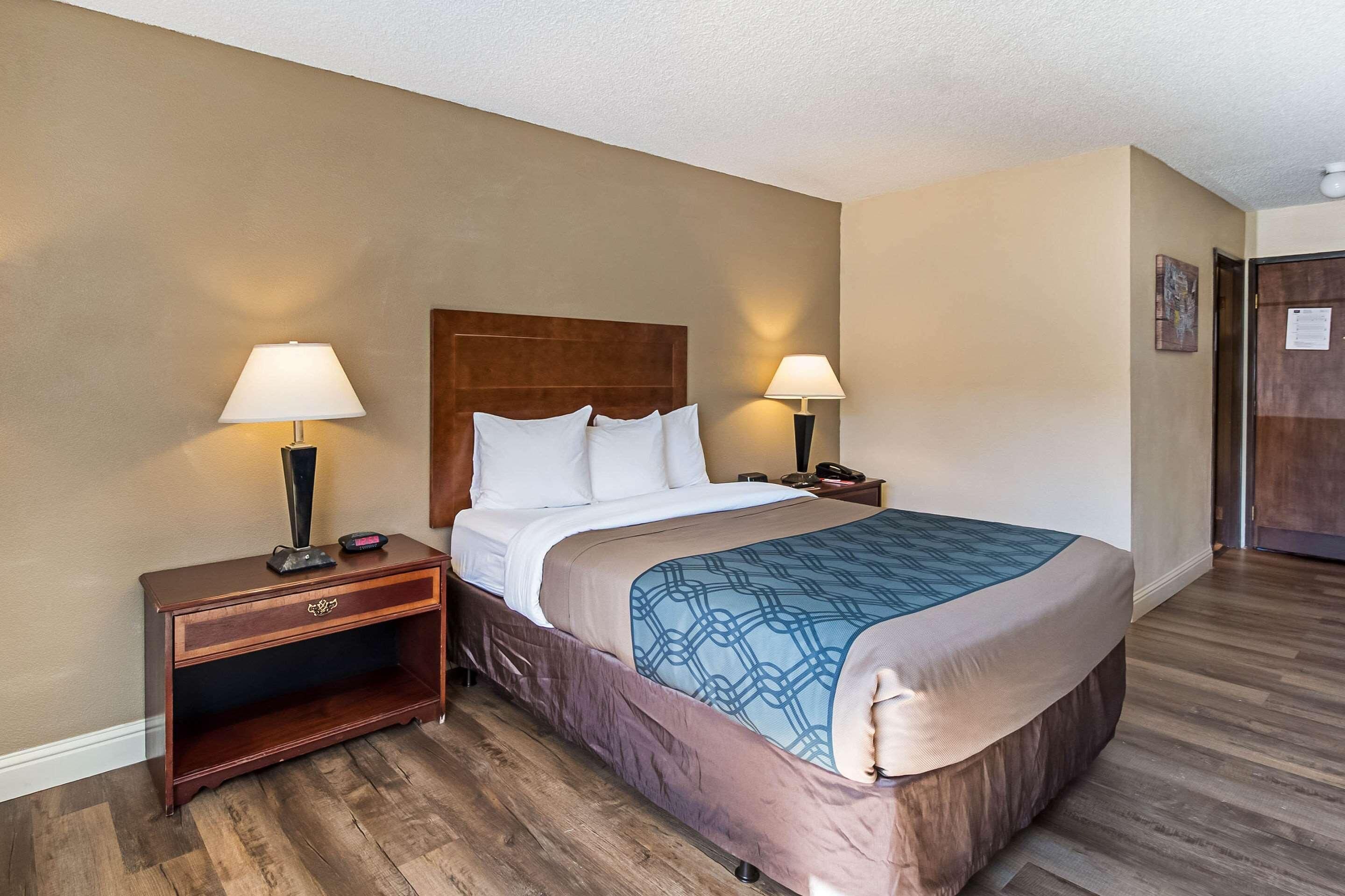 Habitación de hotel con una cama grande, dos lámparas de noche, una mesita de madera y una puerta a la derecha.