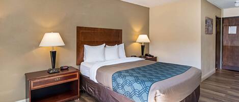 Habitación de hotel con una cama grande, dos lámparas de noche, una mesita de madera y una puerta a la derecha.