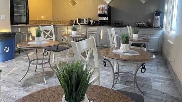Une cuisine moderne avec des meubles blancs, un coin repas doté de tables rondes et de chaises blanches, et une grande fenêtre laissant entrer la lumière naturelle.