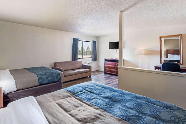 A hotel room with two beds, a sofa, a desk with a lamp, a dresser, and a window with curtains. - Sutter Inn (Yuba City)