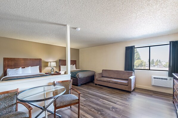 A hotel room with a bed, a sofa, a glass table with chairs, and a window with curtains. - Sutter Inn (Yuba City)