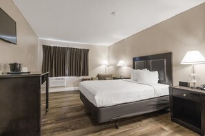 A hotel room with a bed, bedside tables, lamps, a flat-screen TV, a desk with a computer, and a window with curtains. - Sutter Inn (Yuba City)