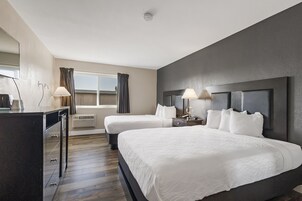 A hotel room with two beds, a desk, and a window with curtains.