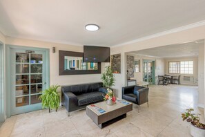 A spacious lobby with a dark leather sofa, a coffee table with a flower vase, and a flat-screen TV mounted on the wall. - Hotel Avenida - Oceanside Camp Pendleton (Oceanside)