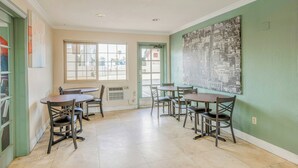 A dining area with tables and chairs, a window with a view, and a door with a green frame. - Hotel Avenida - Oceanside Camp Pendleton (Oceanside)
