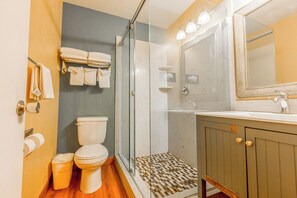 A bathroom with a toilet, a shower with a glass door, a sink, and a mirror. - Hotel Avenida - Oceanside Camp Pendleton (Oceanside)