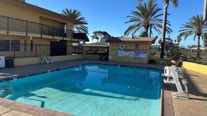 A swimming pool with a clear blue water, surrounded by a building with a balcony and palm trees. - Hotel Avenida - Oceanside Camp Pendleton (Oceanside)