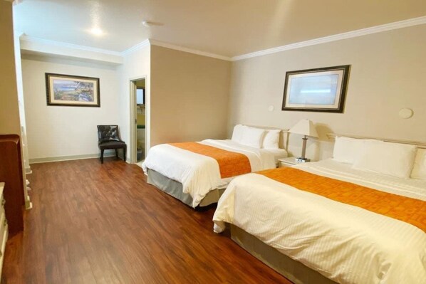 A hotel room with two beds, wooden flooring, a chair, and framed pictures on the walls. - Monarch Valley Inn Marina at Monterey Bay (Marina)