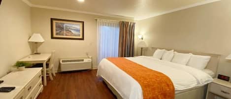 Habitación de hotel con cama, mesita de noche, lámpara, escritorio, silla y unidad de aire acondicionado.
