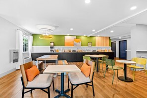 A modern kitchen with a green accent wall, wooden cabinets, and a variety of seating options including tables and chairs. - Spark by Hilton Modesto (Modesto)