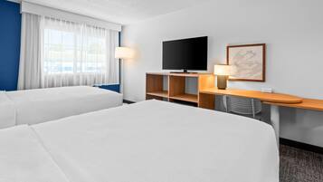 A hotel room with two beds, a TV, a desk, and a chair.