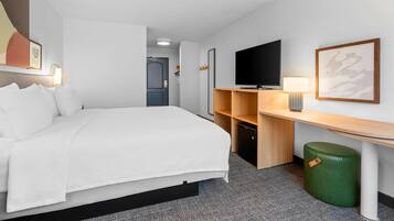 Quarto de hotel com uma cama, televisão, escrivaninha e lixeira.
