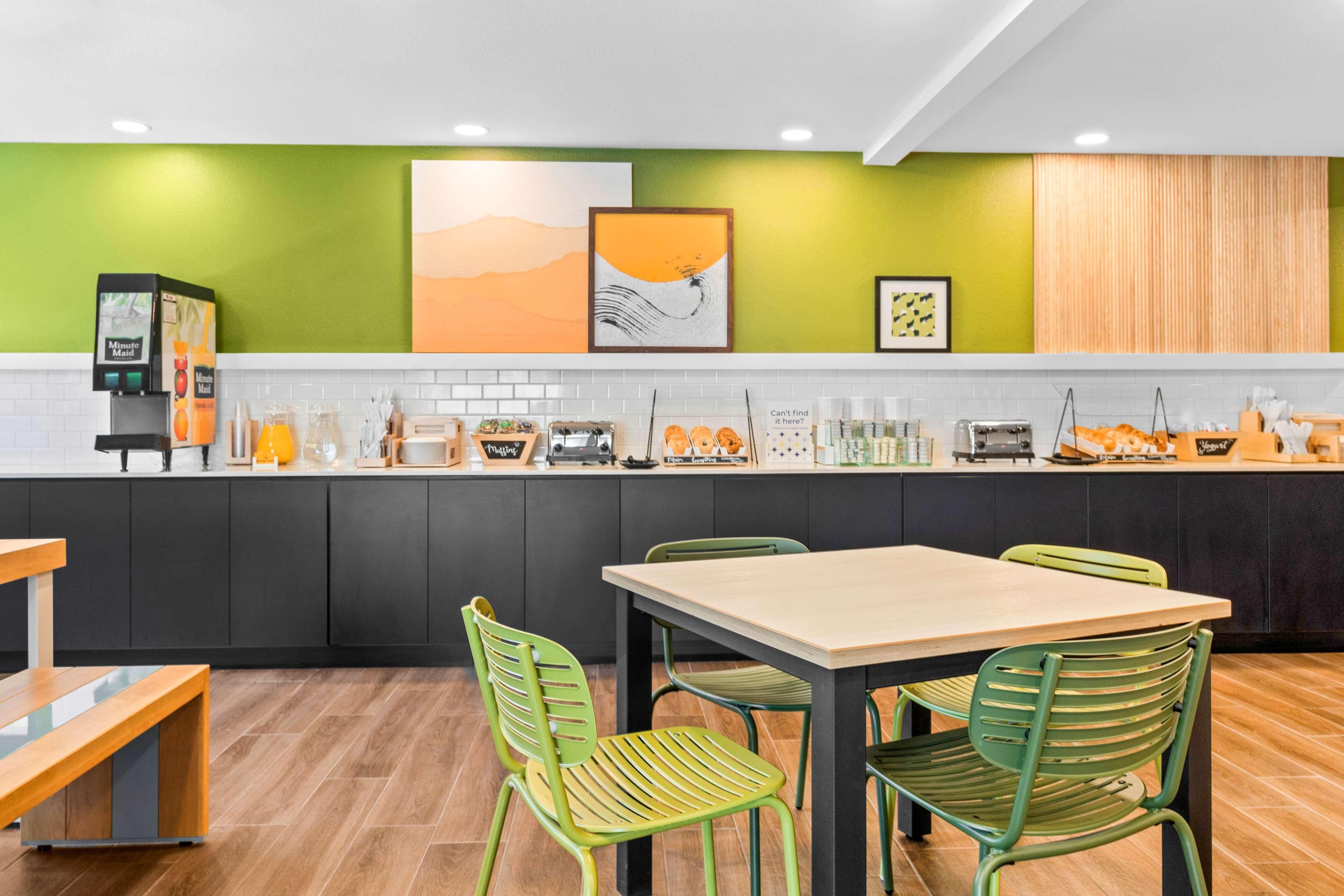 A modern kitchen with a green accent wall, a coffee machine, and a dining area with green chairs.