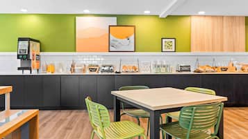 A modern kitchen with a green accent wall, a coffee machine, and a dining area with green chairs.