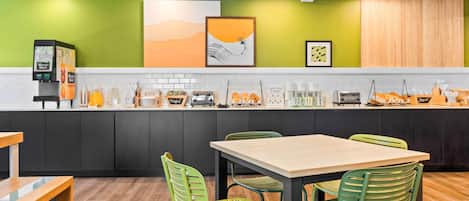 A modern kitchen with a green accent wall, a coffee machine, and a dining area with green chairs.