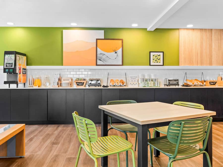 A modern kitchen with a green accent wall, a coffee machine, and a dining area with green chairs.
