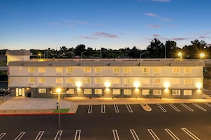 Un hotel de varios pisos con una fila de habitaciones, un estacionamiento y farolas.