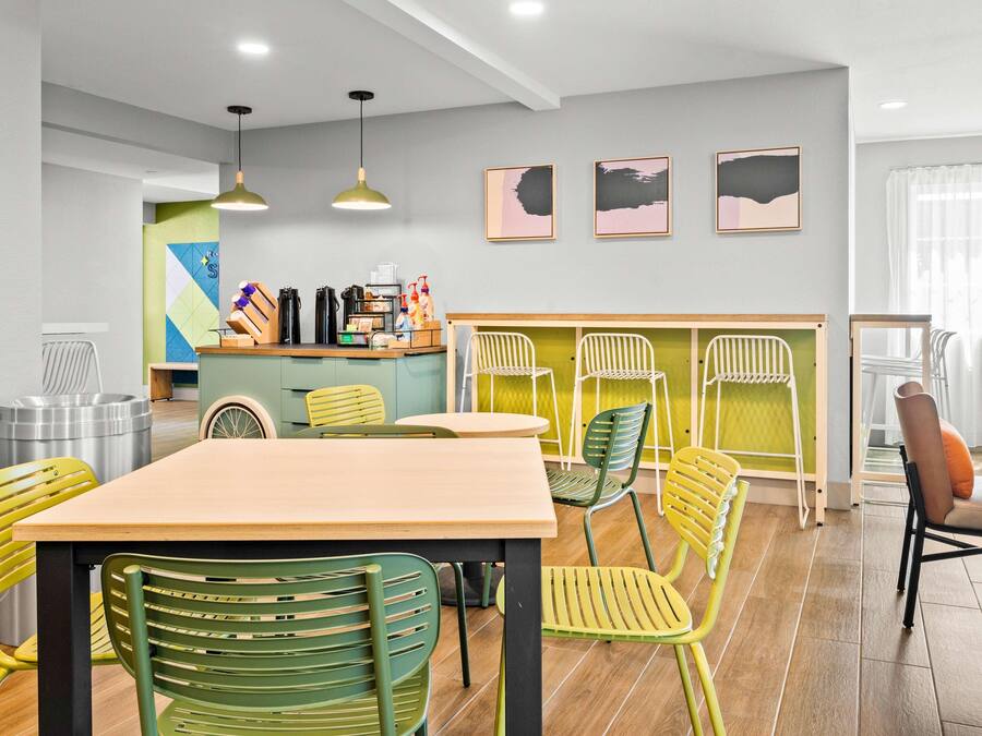 A dining area with a wooden table and green chairs, a kitchen area with a counter and various items, and a window with curtains.
