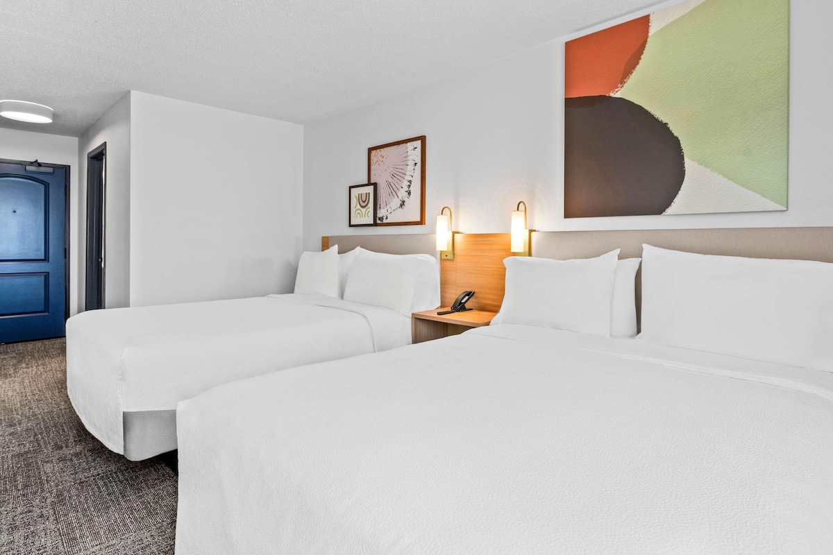 Quarto de hotel com duas camas, uma cabeceira de madeira, um telefone fixado na parede e uma porta.