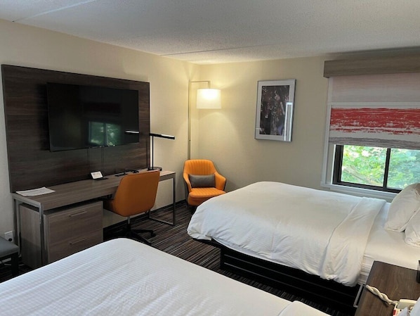 A hotel room with two beds, a desk with a chair, a TV, a lamp, and a window with a view. - Rodeway Inn Little Falls NY (Little Falls)