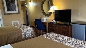 A hotel room with two beds, a desk with a chair, a television, a mirror, and a small refrigerator.